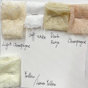 May include: A selection of lace fabric samples in shades such as light champagne, off-white, dark beige, champagne, yellow, and lemon yellow. The swatches are displayed on a white surface, with handwritten colour labels.