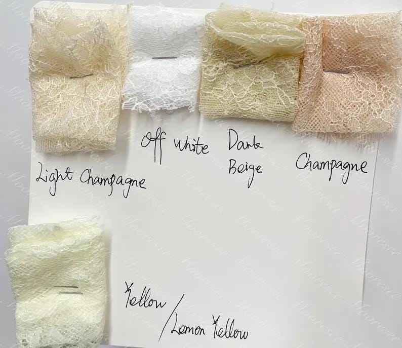 May include: A selection of lace fabric samples in shades such as light champagne, off-white, dark beige, champagne, yellow, and lemon yellow. The swatches are displayed on a white surface, with handwritten colour labels.