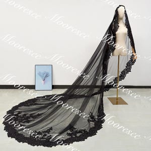 May include: A long, black bridal veil with intricate lace detailing along the edges. The veil is displayed on a mannequin, showcasing its flowing design and delicate craftsmanship. The veil's train extends across the floor, highlighting its length and elegance.