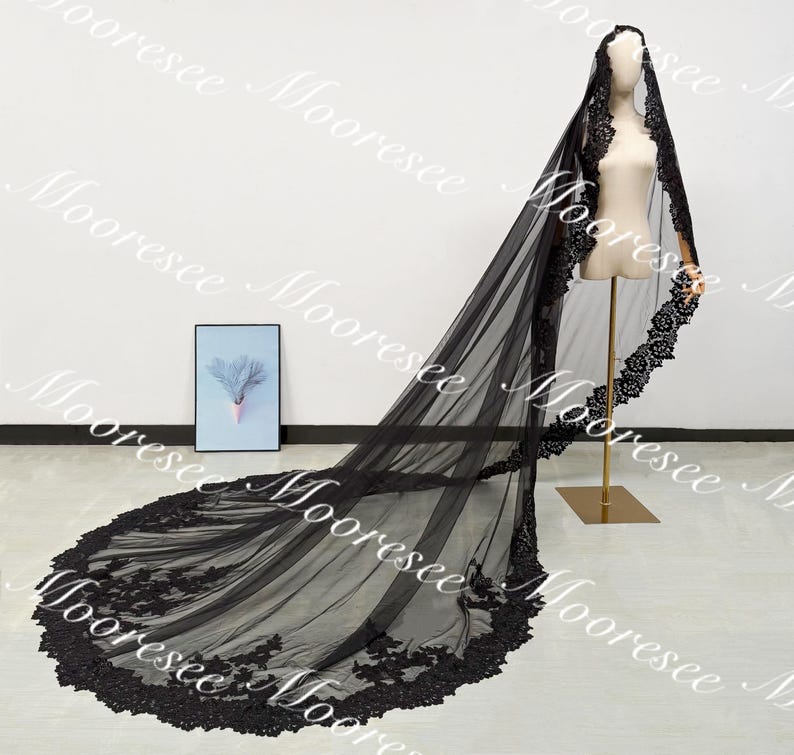 May include: A long, black bridal veil with intricate lace detailing along the edges. The veil is displayed on a mannequin, showcasing its flowing design and delicate craftsmanship. The veil's train extends across the floor, highlighting its length and elegance.