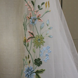 May include: White sheer fabric with embroidered floral design. The flowers are in shades of pink, blue, green, and yellow.