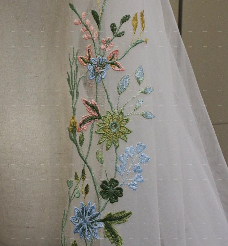 May include: White sheer fabric with embroidered floral design. The flowers are in shades of pink, blue, green, and yellow.
