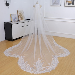Peut inclure: Un long voile de mariée blanc avec des détails de dentelle florale délicate sur le bord inférieur. Le voile est présenté sur un mannequin, mettant en valeur son tissu fluide et transparent. La dentelle ajoute une touche d'élégance à l'accessoire de mariage.
