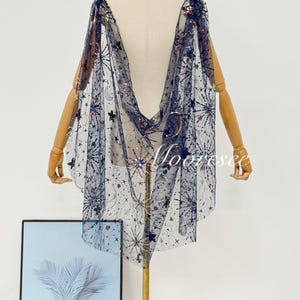 May include: A navy blue cape with a celestial design, featuring stars, moons, and other celestial elements. The cape is made of a sheer fabric and is embellished with sequins. The word "Moorssee" is visible on the bottom right.