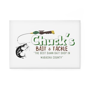 Könnte beinhalten: Ein weißes Schild mit grünem Text, auf dem "Chuck's Bait & Tackle" und der Slogan "The Best Damn Bait Shop in Wabasha County" steht. Ein Cartoon-Bild eines Fisches, der an einer Angelschnur mit einer Entenattrappe am Ende der Schnur gefangen wird.