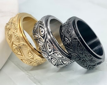May include: Three spinning rings with an eye design. The rings are gold, silver, and black.