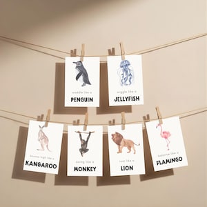 A collection of animal-themed art prints, each featuring a watercolor illustration and a descriptive phrase. The prints are suspended by clothespins on a string. Animals include a penguin, jellyfish, kangaroo, monkey, lion, and flamingo.