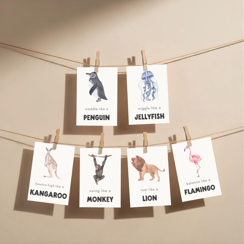 A collection of animal-themed art prints, each featuring a watercolor illustration and a descriptive phrase. The prints are suspended by clothespins on a string. Animals include a penguin, jellyfish, kangaroo, monkey, lion, and flamingo.