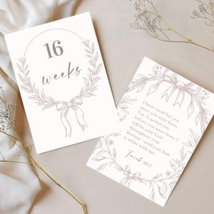 May include: Two cream-coloured cards with floral and bow illustrations. One card reads "16 weeks" inside a wreath. The other card has a quote from Isaiah 46:3. The cards are on a cream-coloured fabric background.