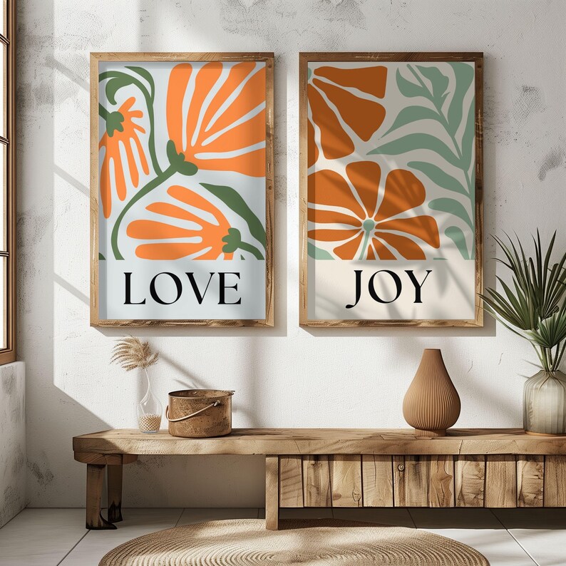 Set of two abstract floral wall art prints featuring “LOVE” and “JOY” in bold text with earthy orange and green tones, styled in a boho wooden frame setup.