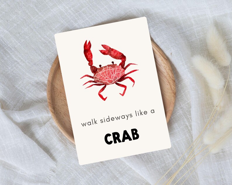 A 5x7 portrait flashcard with a trendy, bright red crab. The card reads, “walk sideways like a crab”. The card sits on top of a wooden bowl, which is on top of white linen.