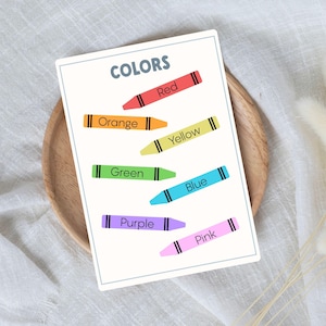 A white card with the word "COLORS" and crayon illustrations in red, orange, yellow, green, blue, purple, and pink. Each crayon is labeled with its respective color name.