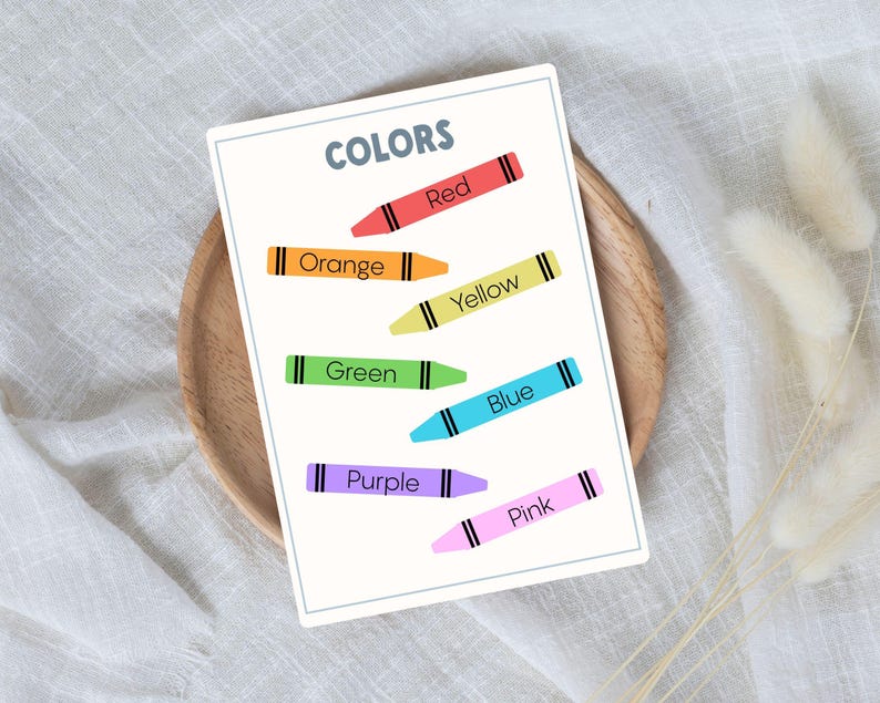 A white card with the word "COLORS" and crayon illustrations in red, orange, yellow, green, blue, purple, and pink. Each crayon is labeled with its respective color name.