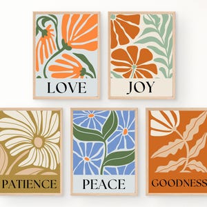 Five floral prints featuring various flower designs and colors, including orange, blue, and gold. Each print includes a word: LOVE, JOY, PATIENCE, PEACE, and GOODNESS. The prints are framed in light wood and have a minimalist aesthetic.