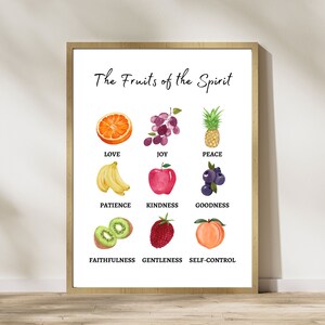 A white poster with a brown frame. The poster has the title 'The Fruits of the Spirit' in black text. Below the title are nine rows of images and text. Each row has a fruit image and a word. The fruits are an orange slice, grapes, a pineapple, bananas, an apple, blueberries, a kiwi, a raspberry, and a peach. The words are 'Love', 'Joy', 'Peace', 'Patience', 'Kindness', 'Goodness', 'Faithfulness', 'Gentleness', and 'Self-Control'.