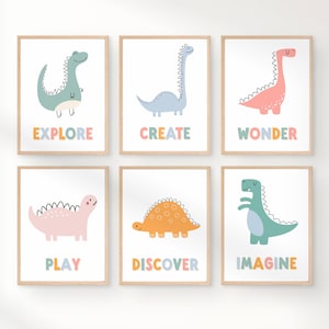 May include: Six framed art prints featuring colorful cartoon dinosaurs. Each print has a different dinosaur in shades of blue, pink, and orange, with a word below: Explore, Create, Wonder, Play, Discover, and Imagine. The prints have a white background and a light wood frame.