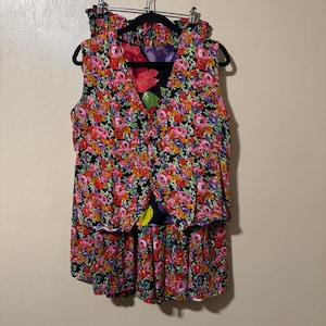 May include: A sleeveless vest and a matching skirt set featuring a vibrant floral pattern with red, pink, yellow, and purple flowers on a black background. The vest has a button-front closure, and the skirt features an elasticized waistband.
