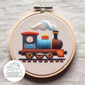 Peut inclure: Art de broderie en forme de cercle représentant un train bleu et marron avec des roues orange et une fumée blanche, bleue et orange. Le train est sur une voie ferrée marron et le cercle est en bois naturel.