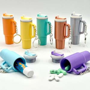 Puede incluir: Una colección de llaveros en miniatura con forma de vaso, de colores brillantes. Los llaveros son de varios colores, incluyendo naranja, amarillo, turquesa, cobre y gris. Algunos llaveros están abiertos, revelando pequeños objetos en su interior.