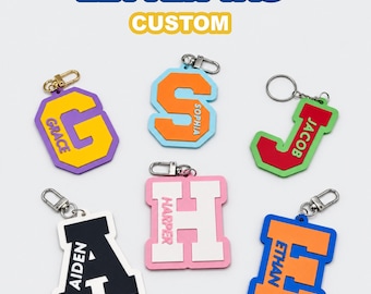 May include: Six custom letter tags featuring the names Grace, Sophia, Jacob, Aiden, Harper, and Ethan. Each tag is a different color combination with a metal lobster clasp or ring. The text LETTER TAG CUSTOM appears at the top of the image.