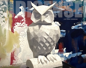 May include: A white, geometric owl sculpture with a speckled finish. The owl is perched on a base and has a detailed, angular design. The sculpture is set against a colorful abstract background.