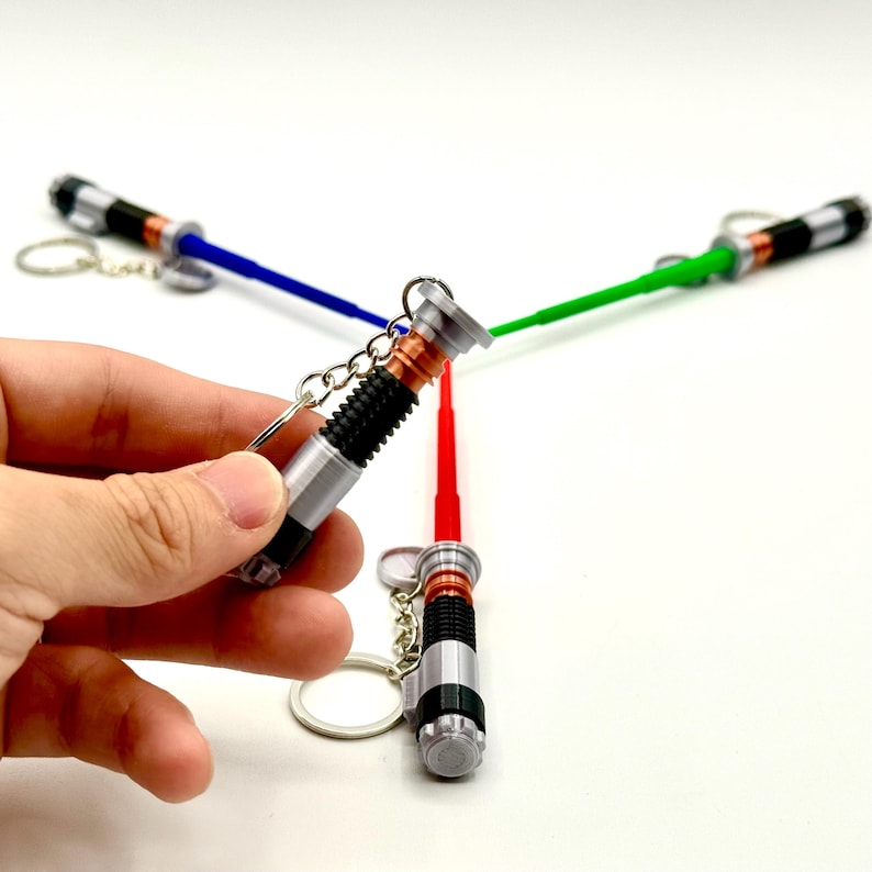 May include: Miniature lightsaber keychains in red, blue, and green. The keychains have silver and black handles with a copper-colored accent. The lightsaber blades are made of plastic and are attached to a silver keyring.