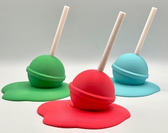 May include: Three colorful lollipops with white sticks are melting into pools of colored paint. The lollipops are green, red, and blue.