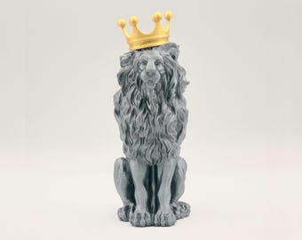 May include: A gray stone lion figurine wearing a gold crown. The lion is sitting with its paws tucked in front of it.