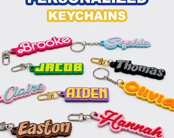 May include: A collection of personalized keychains featuring various names including Brooke, Sophia, Jacob, Thomas, Claire, Aiden, Olivia, Easton, and Hannah. Each keychain displays a name in a unique color, font, and style with a metal ring.