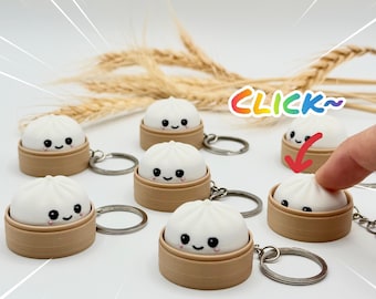 May include: A collection of white dumpling keychains, each featuring a smiling face and resting inside a small, tan, cylindrical steamer basket. The keychains include a metal ring attachment. The text CLICK~ is visible in rainbow colors.