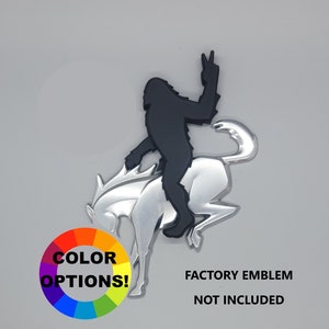 May include: A black silhouette of Bigfoot giving a peace sign riding a silver horse emblem. The words "COLOR OPTIONS!" are displayed with a color wheel. The text "FACTORY EMBLEM NOT INCLUDED" is also present.