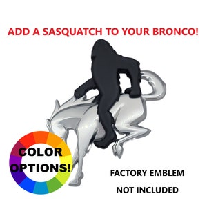 May include: A black Sasquatch figure riding a silver Bronco emblem. The text "ADD A SASQUATCH TO YOUR BRONCO!" is above the emblem. A color wheel with "COLOR OPTIONS!" is on the left. The text "FACTORY EMBLEM NOT INCLUDED" is below.