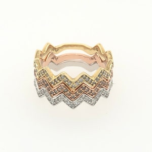 May include: Stackable rings in gold, rose gold, and silver tones. Each ring features a zigzag design, with the bottom ring encrusted with clear gemstones. The rings are displayed on a white background.