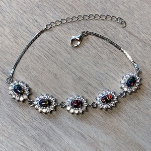 Könnte beinhalten: Ein silbernes Armband mit vier ovalen schwarzen Opalen, die in einem silbernen Rahmen mit klaren Zirkonia-Steinen gefasst sind. Das Armband hat eine silberne Kette mit einem Karabinerverschluss.