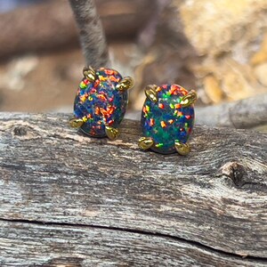 May include: A pair of gold opal earrings with a black and iridescent opal stone in each earring.