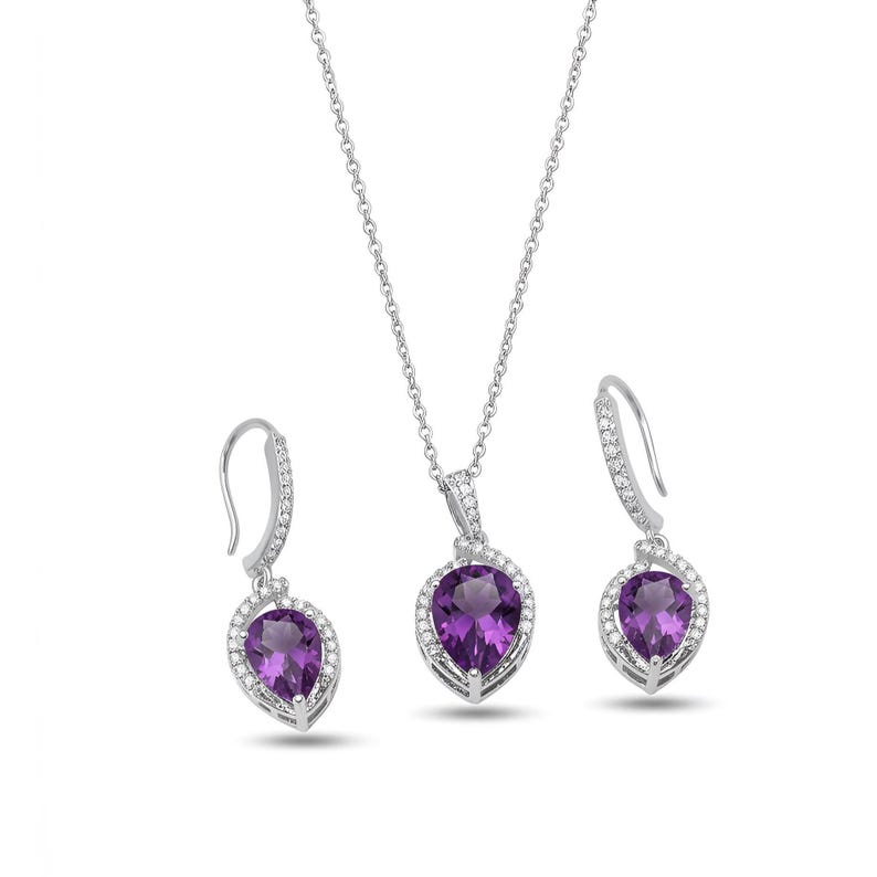 K&ouml;nnte beinhalten: Ein Schmuckset bestehend aus einer silbernen Halskette und zwei passenden Ohrh&auml;ngern. Jedes St&uuml;ck zeigt einen birnenf&ouml;rmigen violetten Amethyst, der von einem Kranz aus kleinen wei&szlig;en Steinen umgeben ist und an silbernen Ketten und Haken h&auml;ngt.