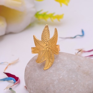 May include: A gold-toned ring featuring a leaf-shaped design. The ring is crafted from metal and has a textured finish.