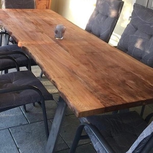 Peut inclure: Une grande table en bois avec un plateau &agrave; bord vif et des pieds en m&eacute;tal noir. La table est entour&eacute;e de six chaises noires avec des coussins gris.