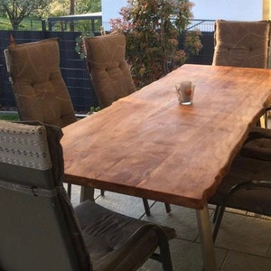 Peut inclure: Une table en bois avec un bord brut, entour&eacute;e de chaises avec des coussins bruns. La table est en bois brun clair et a un aspect naturel et rustique.