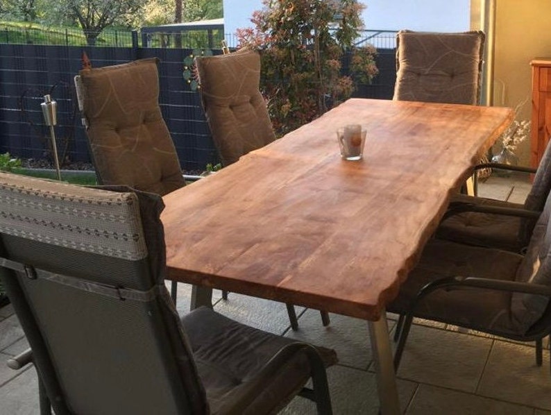 Peut inclure: Une table en bois avec un bord brut, entour&eacute;e de chaises avec des coussins bruns. La table est en bois brun clair et a un aspect naturel et rustique.