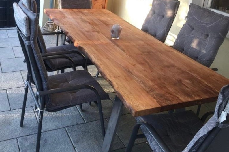 Peut inclure: Une grande table en bois avec un plateau &agrave; bord vif et des pieds en m&eacute;tal noir. La table est entour&eacute;e de six chaises noires avec des coussins gris.