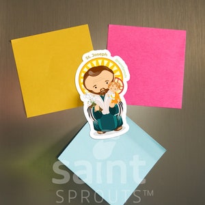May include: A colorful illustrated magnet featuring Saint Joseph holding baby Jesus. The magnet is on a silver refrigerator with yellow, pink, and blue sticky notes. The magnet has the text "St. Joseph" and "@saint sprouts" on it.