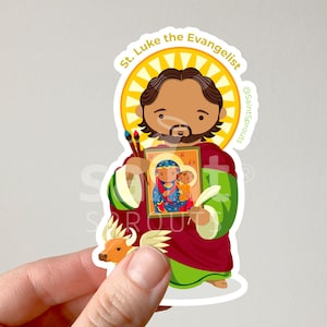 May include: A colorful sticker featuring a cartoon illustration of Saint Luke the Evangelist, holding a paintbrush and a painting of the Virgin Mary and baby Jesus. The sticker has a yellow halo around the saint's head and a white background.