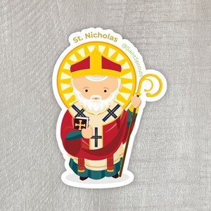 May include: A sticker featuring a cartoon illustration of Saint Nicholas, a white-bearded man wearing a red and gold bishop's robe, holding a book and a staff. The sticker has a yellow halo around his head and the text "St. Nicholas" and "@SaintSprouts" on it.