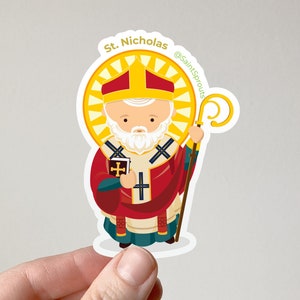 May include: A sticker featuring a cartoon illustration of Saint Nicholas, a white-bearded man wearing a red and gold bishop's robe, holding a book and a staff. The sticker has a yellow halo and the text "St. Nicholas @SaintSprouts" around the border.