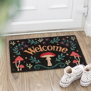 May include: Black doormat featuring a mushroom and floral design, with the word "Welcome" in orange and red mushrooms. The mat is in front of a white door, with white sneakers with black star patterns.