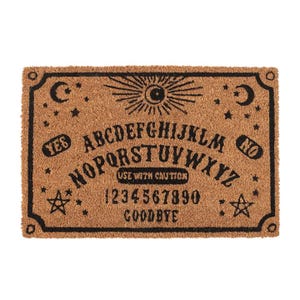 May include: A brown coir doormat with a black outline and a black Ouija board design. The design includes the letters of the alphabet, numbers 1-9 and 0, the words "YES", "NO", "GOODBYE", and "USE WITH CAUTION".