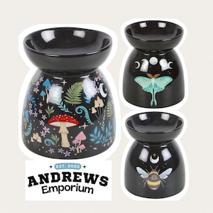 May include: Black ceramic oil warmers with decorative designs. One warmer features a mushroom and floral pattern, another a moth, and the third a bee. The text "ANDREWS Emporium" is at the bottom.