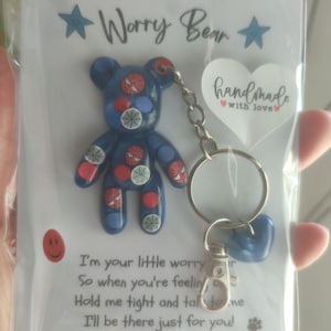 May include: A blue bear-shaped keychain with red and white spider-themed decals, attached to a metal ring and clasp. The item is mounted on a white card featuring the text Worry Bear, handmade with love, and a poem about holding the bear tight.