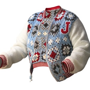 May include: A handmade, crochet varsity jacket with a blue, red, white, and gray granny square design. The jacket features white knit sleeves, a red and white striped trim, and a red "J" patch on the chest.